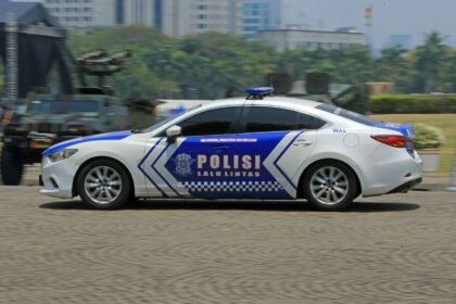 Blue and white Indonesian police car speeding through urban streets in daylight.