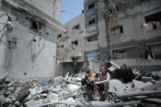 Two boys sit amidst rubble of destroyed buildings.